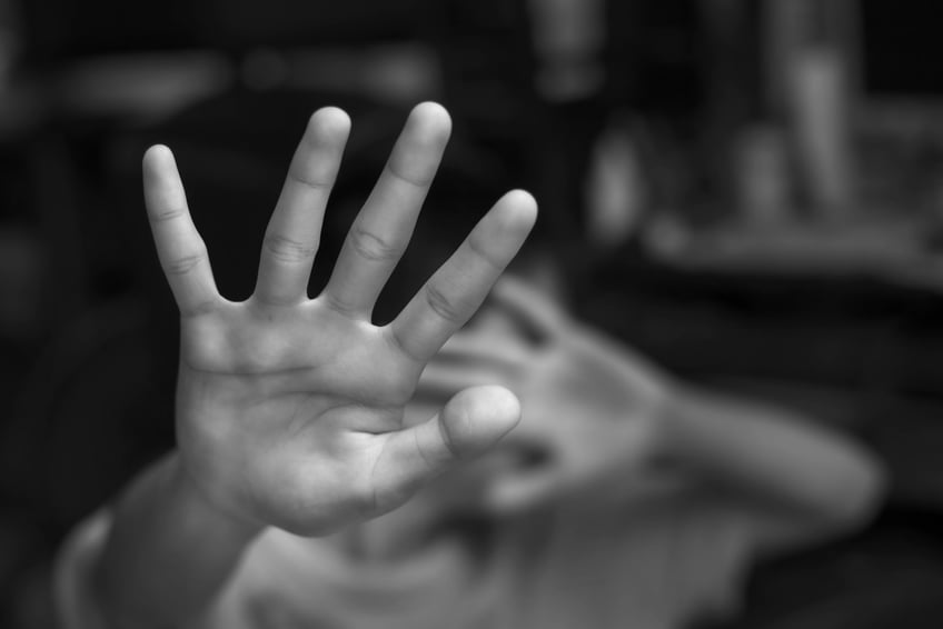 A black-and-white photo depicting a scared child defensively extending arms and hands.